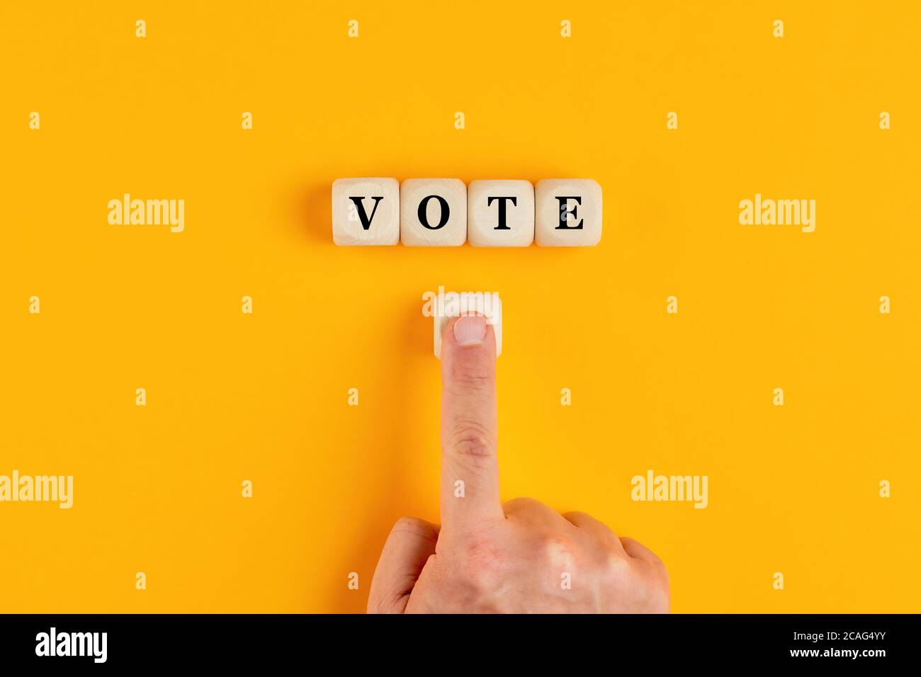 Das Wort Vote auf Holzwürfeln geschrieben mit einer männlichen Hand drücken Sie den Wahlknopf. Online-Wahlkonzept in Politik oder Business-Meetings. Stockfoto