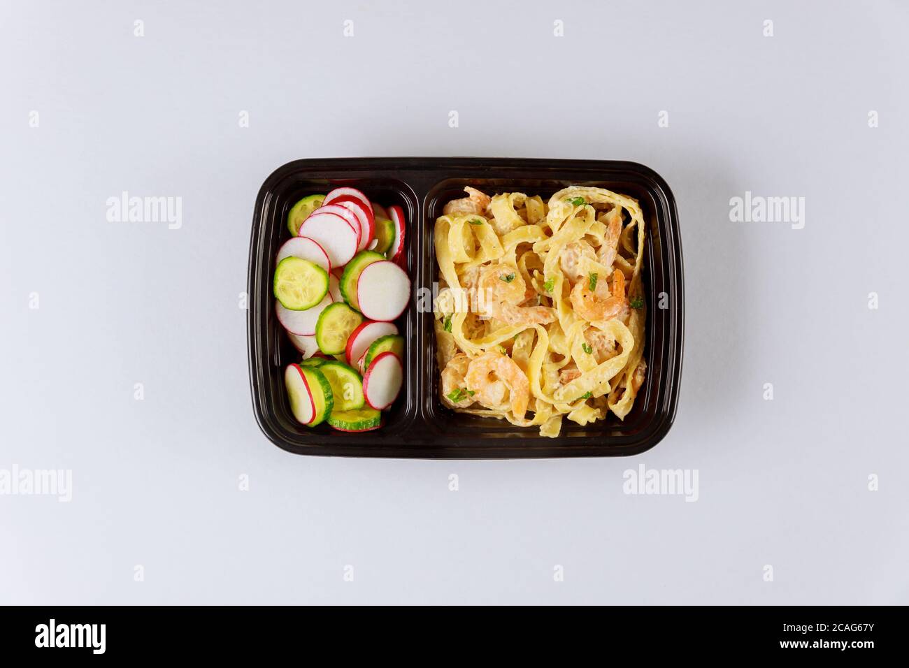 Schwarzer Plastikbehälter mit Nudeln, Garnelen und frischem Salat. Lieferung von Lebensmitteln. Stockfoto