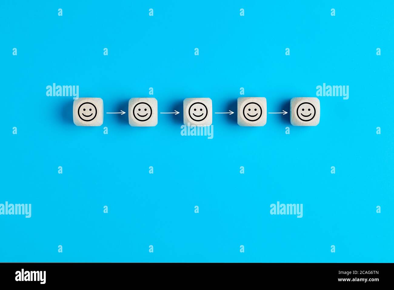 Konzept der sozialen Distanzierung. Holzblöcke mit Smiley-Gesicht-Icons, die durch Pfeile auf blauem Hintergrund entfernt sind. Stockfoto