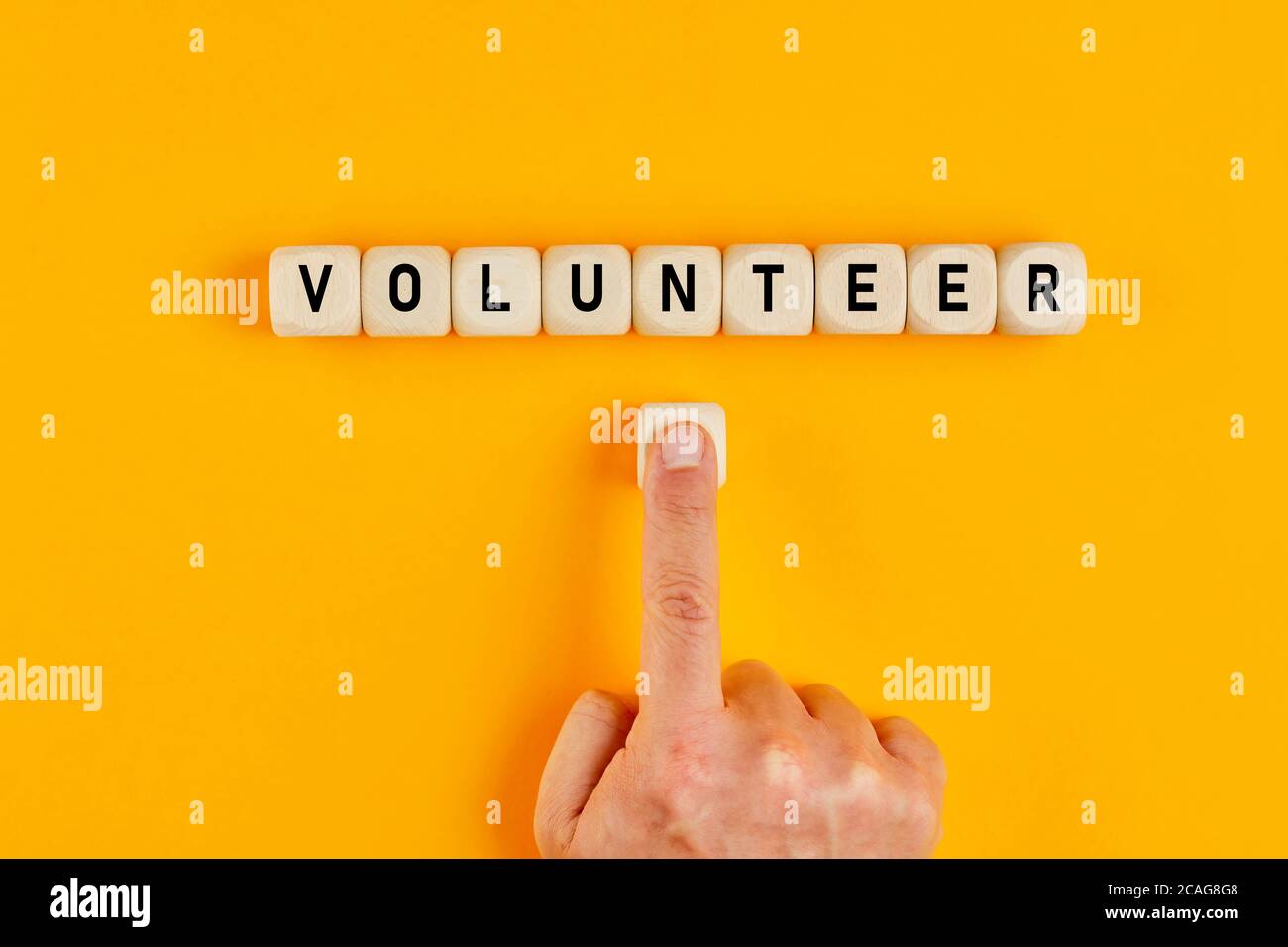 Das Wort Volunteer auf Holzklötze geschrieben, mit einer männlichen Hand, die den Knopf drückt. Konzept der Freiwilligentätigkeit und der Teilnahme an einer Sache. Stockfoto