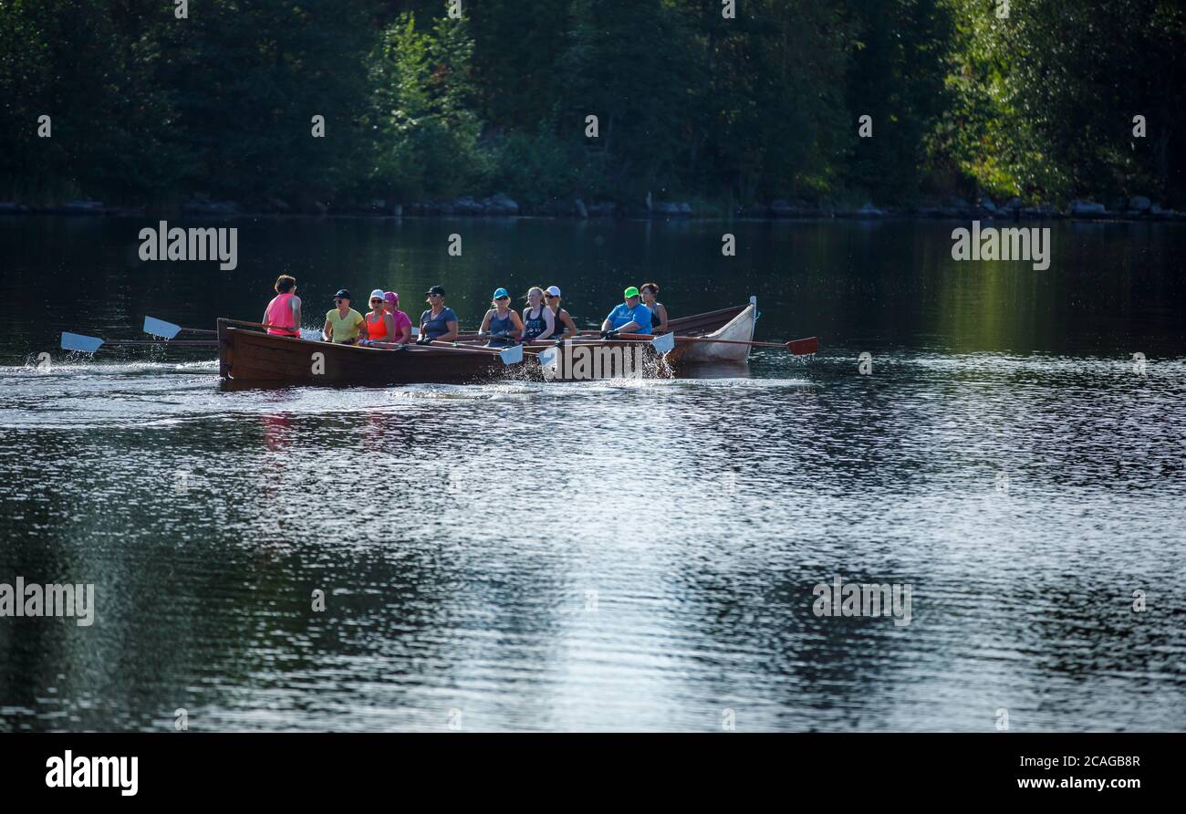 Frauen rudern eine Kopie eines langen hölzernen altmodischen Kirchenbootes mit 9 weiblichen Rudererinnen und weiblichem Bootsmann im Sommer in Finnland Stockfoto