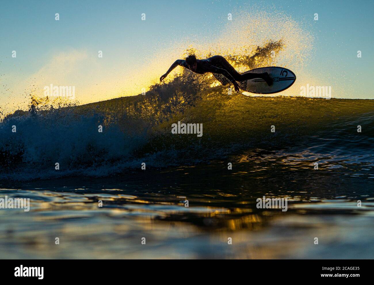 Ein junger Mann in einem Neoprenanzug trifft die Lippe der Welle und führt ein Luftmanöver auf einem Surfbrett durch. Stockfoto