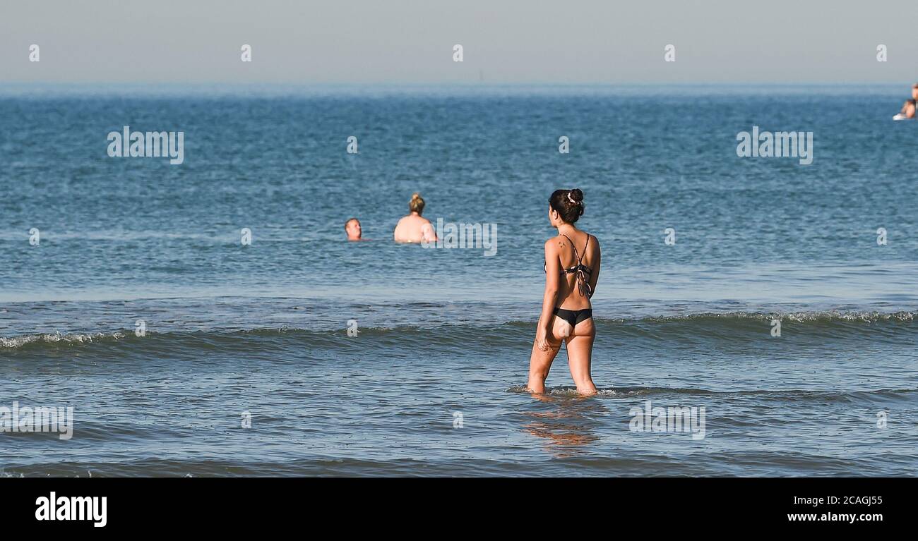 Brighton UK 7. August 2020 - EINE junge Frau geht in das Meer vor Brighton Strand früh am Morgen an einem anderen heißen sonnigen Tag, da die Temperatur prognostiziert wird, um die hohen 30 in einigen Teilen des Südostens heute zu erreichen : Credit Simon Dack / Alamy Live News Stockfoto