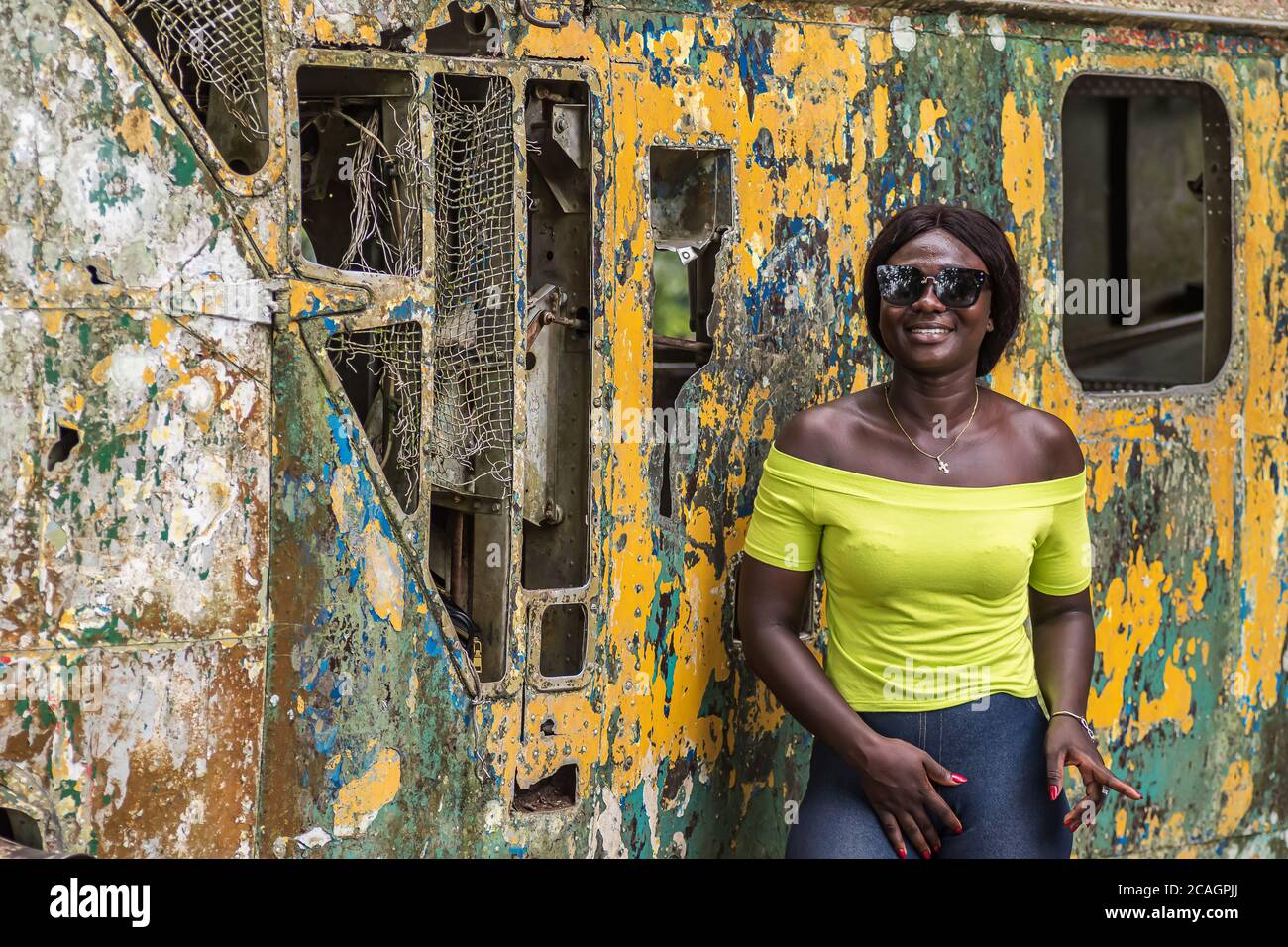 Happy Africa Frau aus Ghana steht vor einem alten zerbrochenen Hubschrauber, der im nördlichen Teil von Accra Ghana Westafrika steht Stockfoto