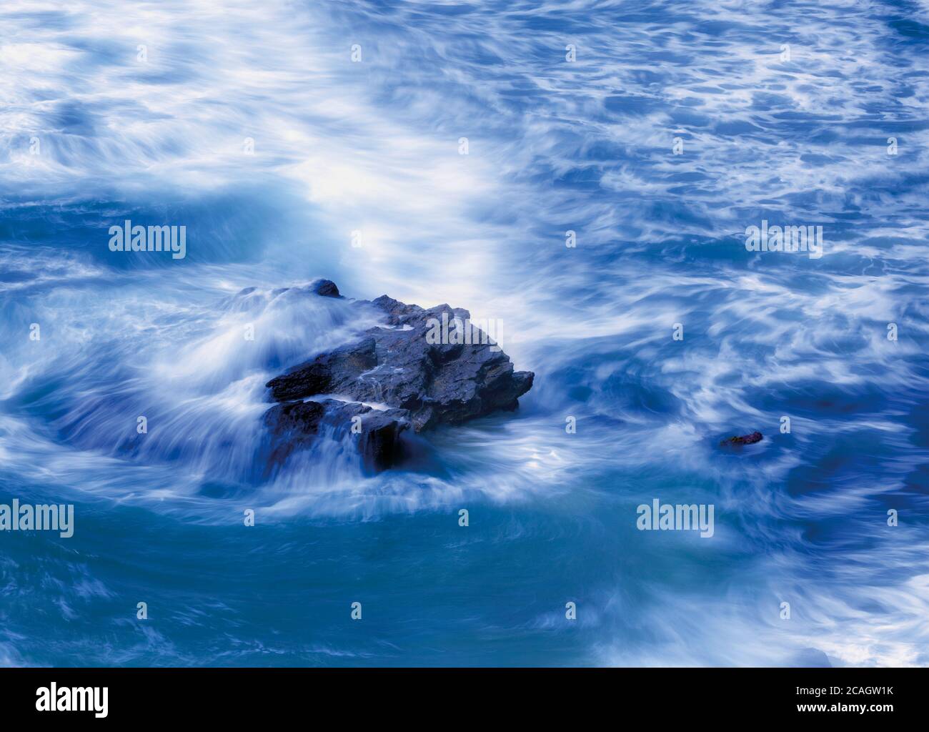 Wasser wirbelt um einen Felsen im Meer herum. Stockfoto