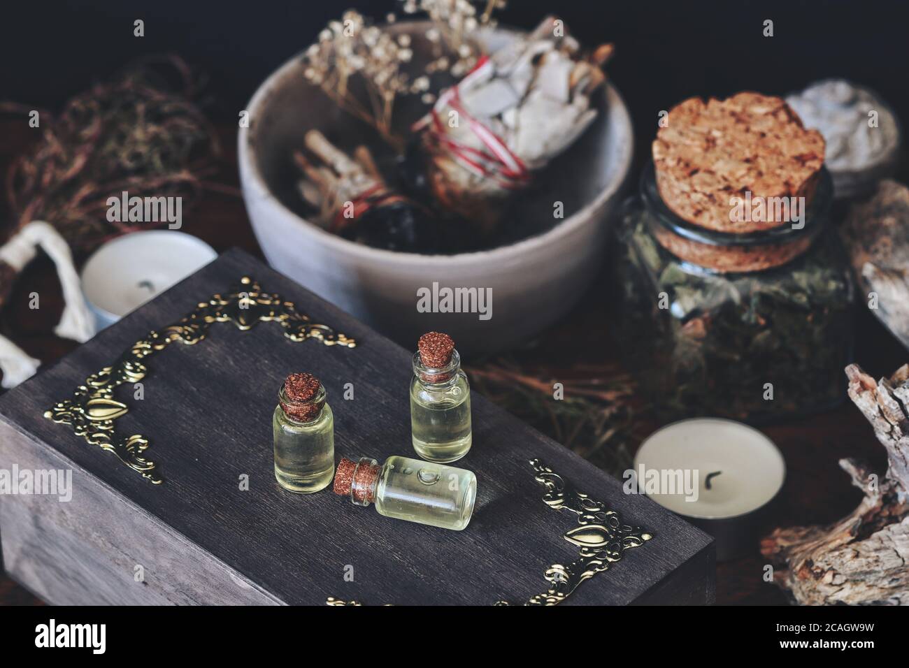 Kleine ätherische Ölflaschen auf dunkelbrauner Holzhexe-Schachtel. Nahaufnahme mit verschiedenen getrockneten Kräutern, Pflanzen, Blumen, Salbei-Wischstock, Kerzen Stockfoto