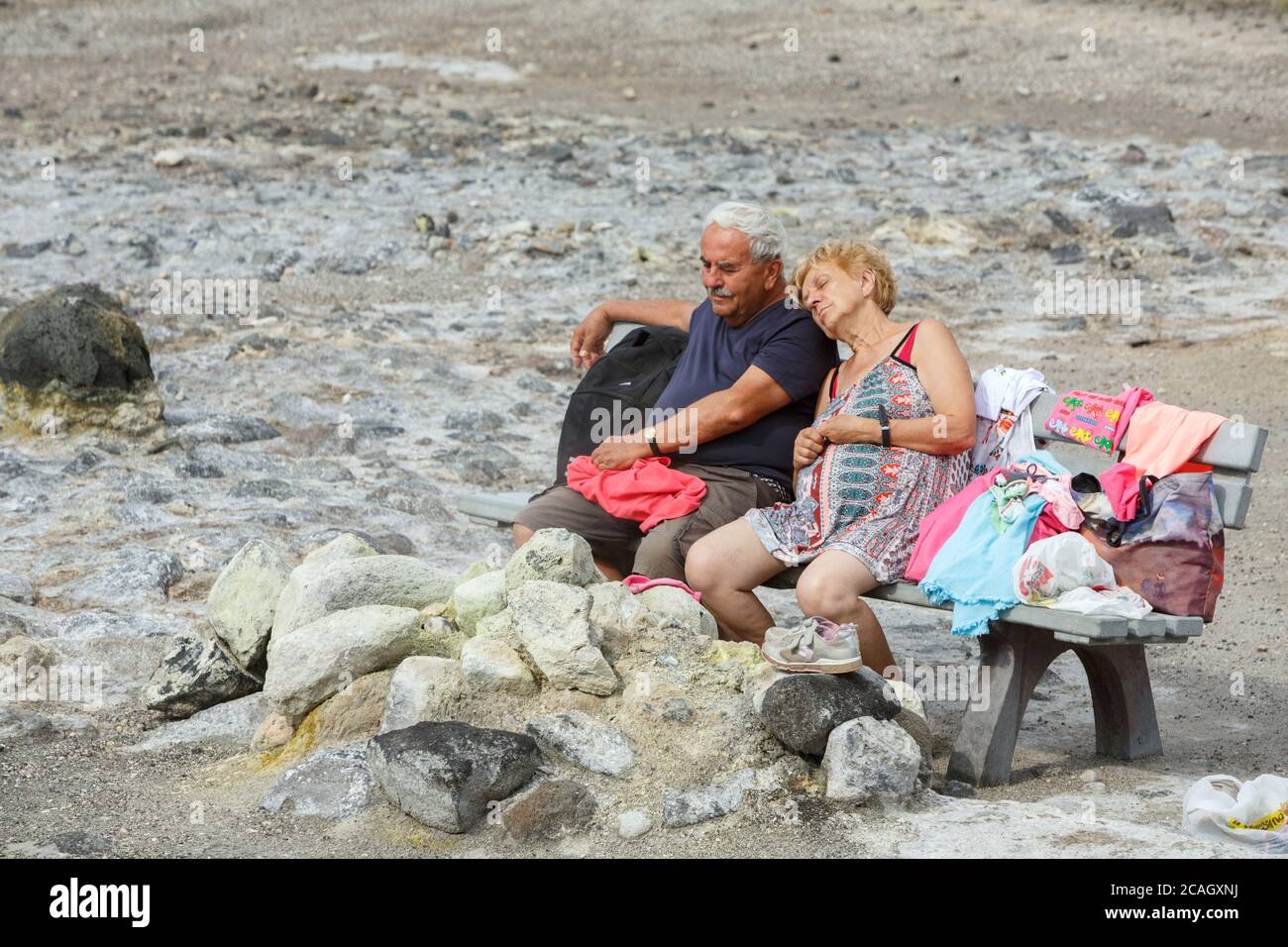 20.08.2018, Vulcano, Sizilien, Italien - ein älteres Paar sitzt mit geschlossenen Augen auf einer Bank und genießt die Hitze und Schwefeldämpfe eines Frühlings Stockfoto
