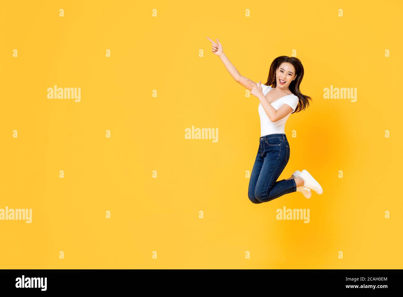 Glücklich lächelnd junge asiatische Mädchen springen mit Händen Poiting nach oben Isoliert auf gelbem Studiohintergrund mit Kopierbereich Stockfoto