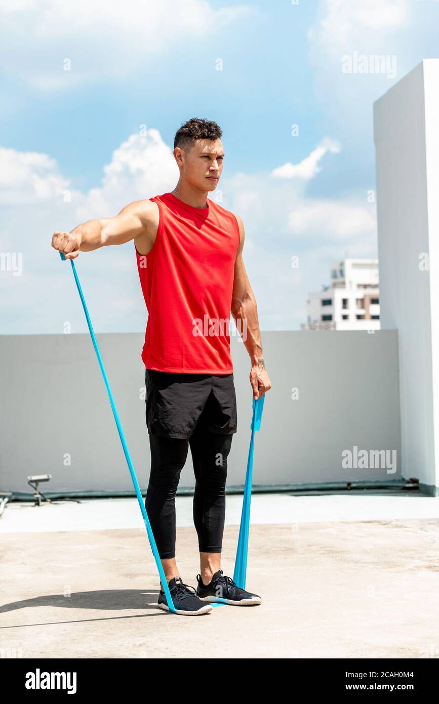 Handsome Sport Mann tun Schulter lateral erhöhen Übung mit Widerstand Band im Freien auf dem Dach in der Sonne Stockfoto
