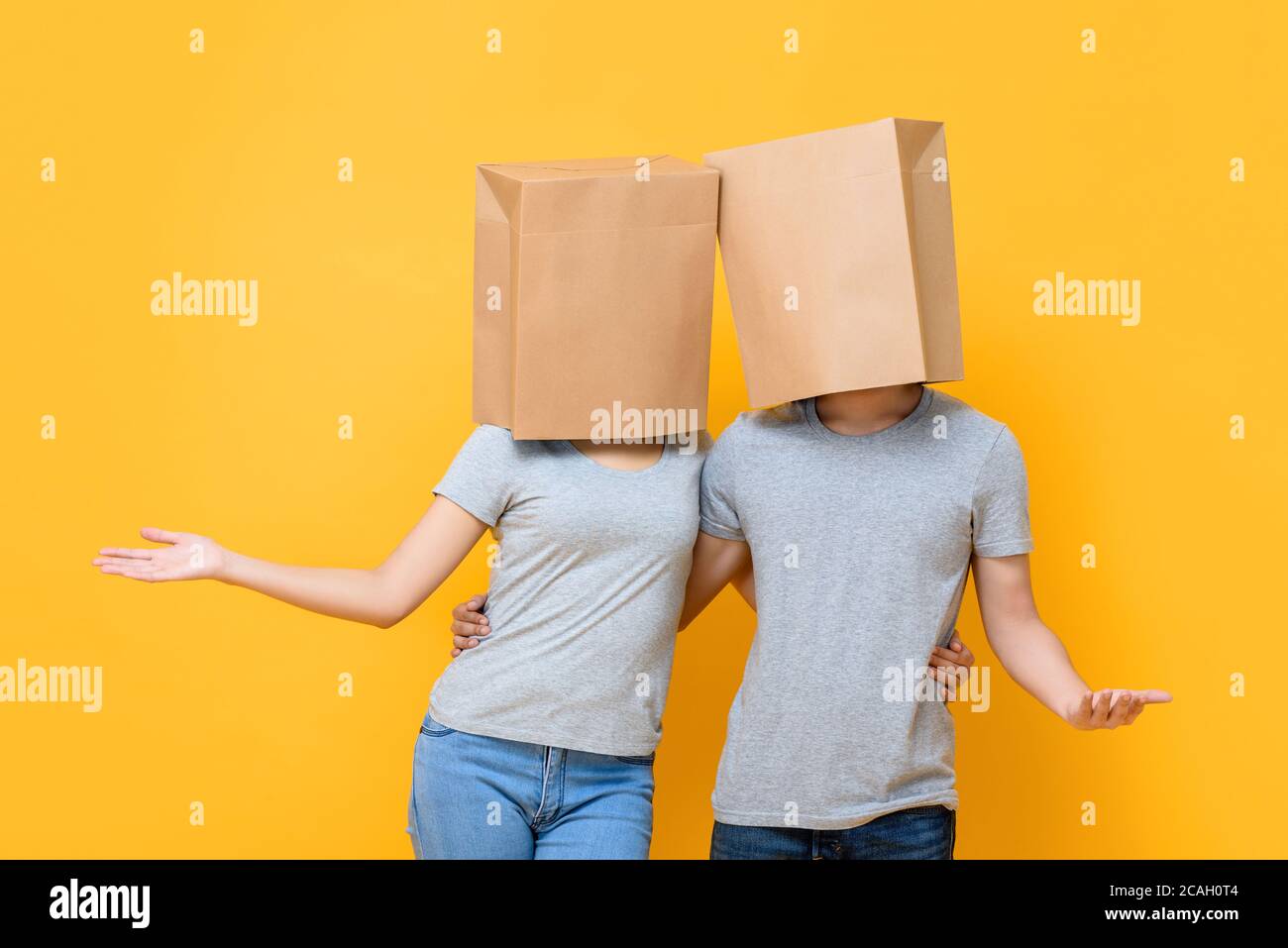 Gesichtsloses anonymes Paar, das Köpfe mit Papiertüten bedeckt und hält Einander tun offene Hand Geste isoliert auf gelben Studio Hintergrund Stockfoto