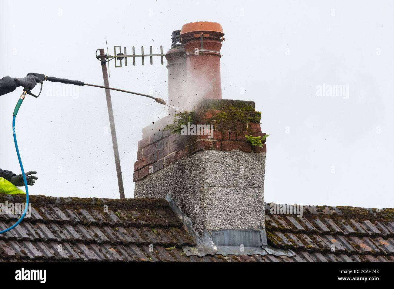 Man macht Waschen einen Schornstein Stapel und Dach zu Schmutz, Moos und kleine Pflanzen zu entfernen - UK Stockfoto