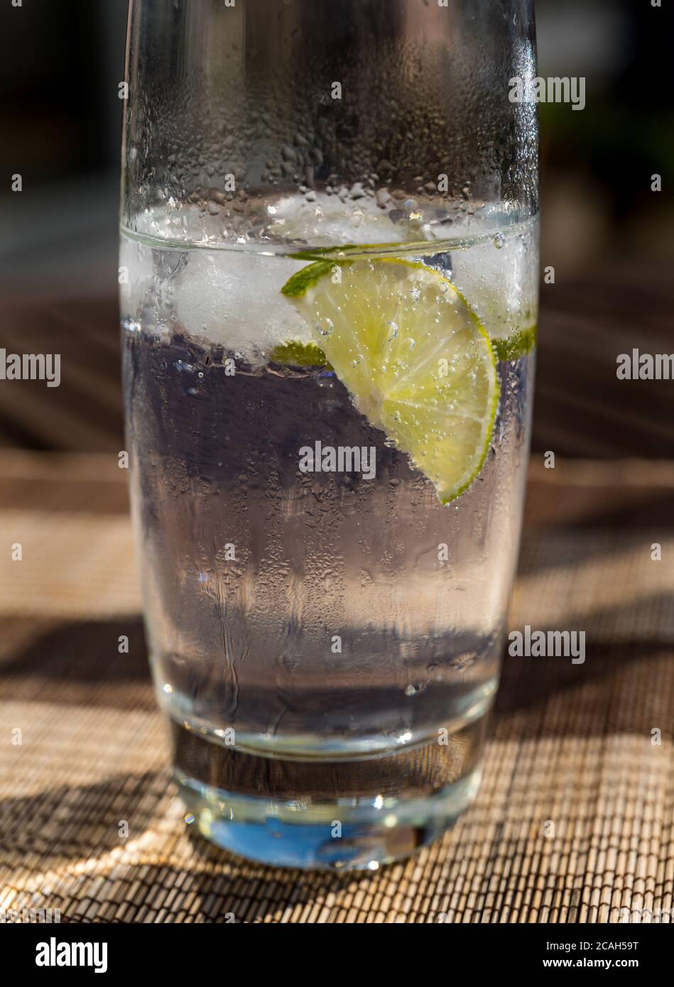 Nahaufnahme von Eis alten Glas mit Gin und Tonic mit Limettenscheiben auf Terrasse Tisch im Freien in der Sonne Stockfoto