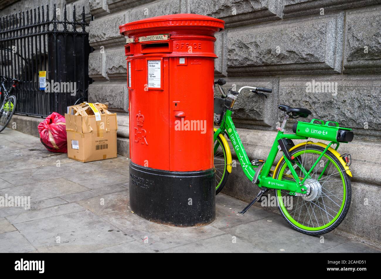 LONDON - 04. FEBRUAR 2020: Ein Leihrad mit Elektroassistent Lime parkte zwischen einer Wand und einer traditionellen roten britischen Post Box mit weggeworfenen Müll Stockfoto