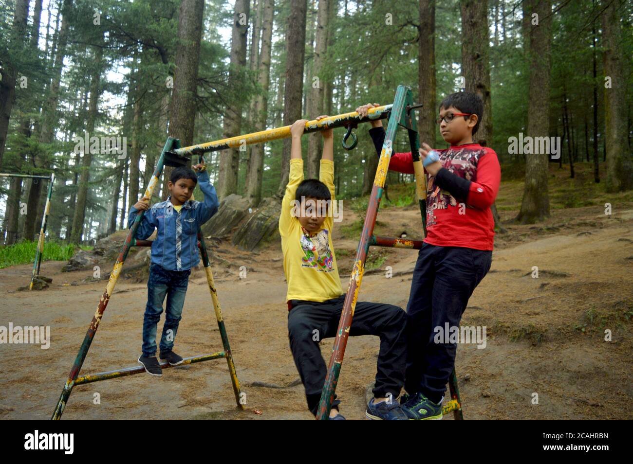 Drei indische Teenager-Jungen, die auf einem pfeifenverspeisten Rahmen einer Schaukel im Park in Manali klettern, genießen die selektive Fokussierung Stockfoto