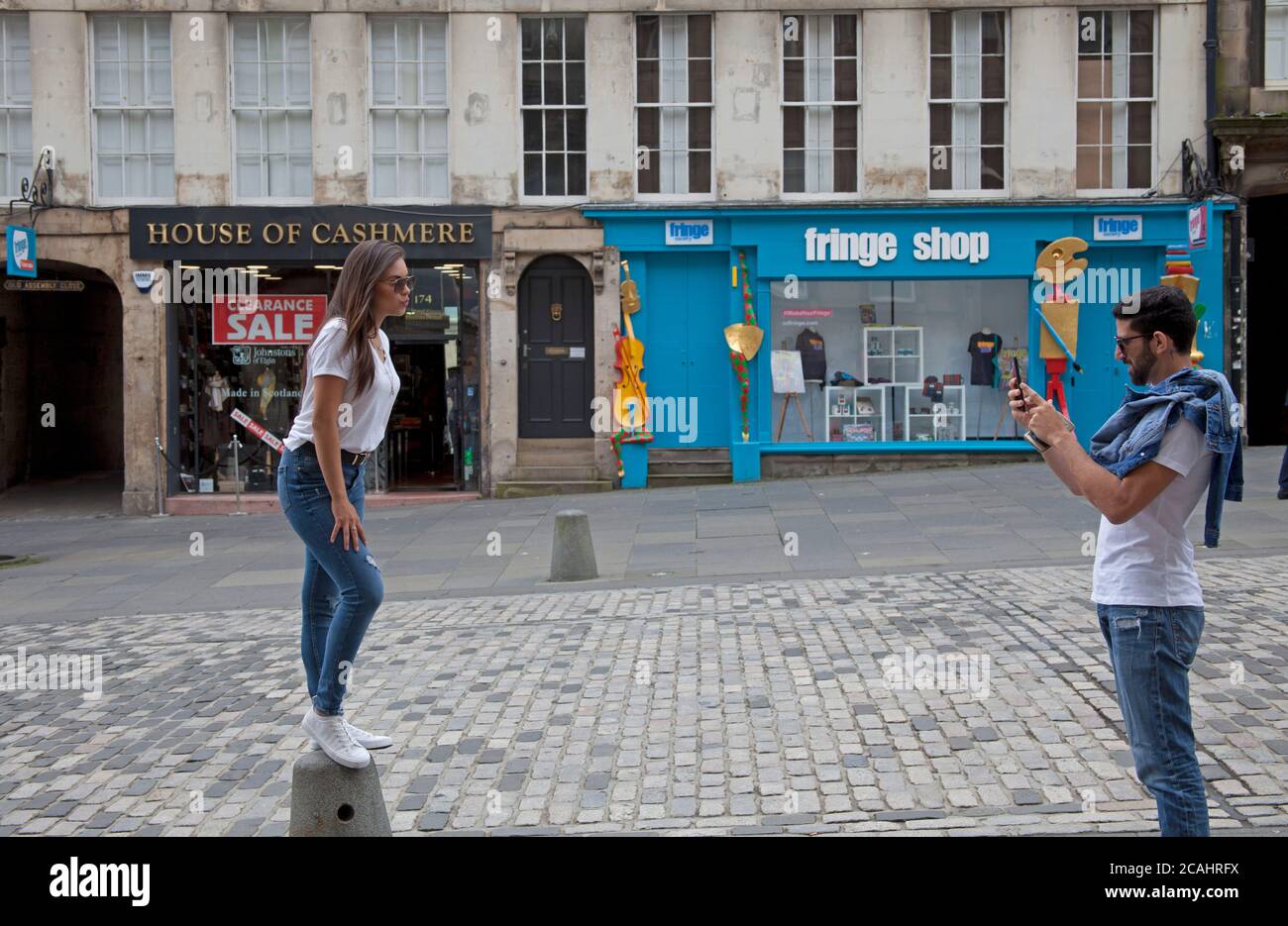 Royal Mile, Edinburgh, Schottland, Großbritannien. August 2020. Bewölkt und schwül 22 Grad. Touristen tröpfeln immer noch in ein einigermaßen ruhiges Stadtzentrum und helfen den Restaurants und Cafés in der schottischen Hauptstadt. Im Bild: Mädchen auf Straßenmöbeln posiert für ein Foto. Stockfoto
