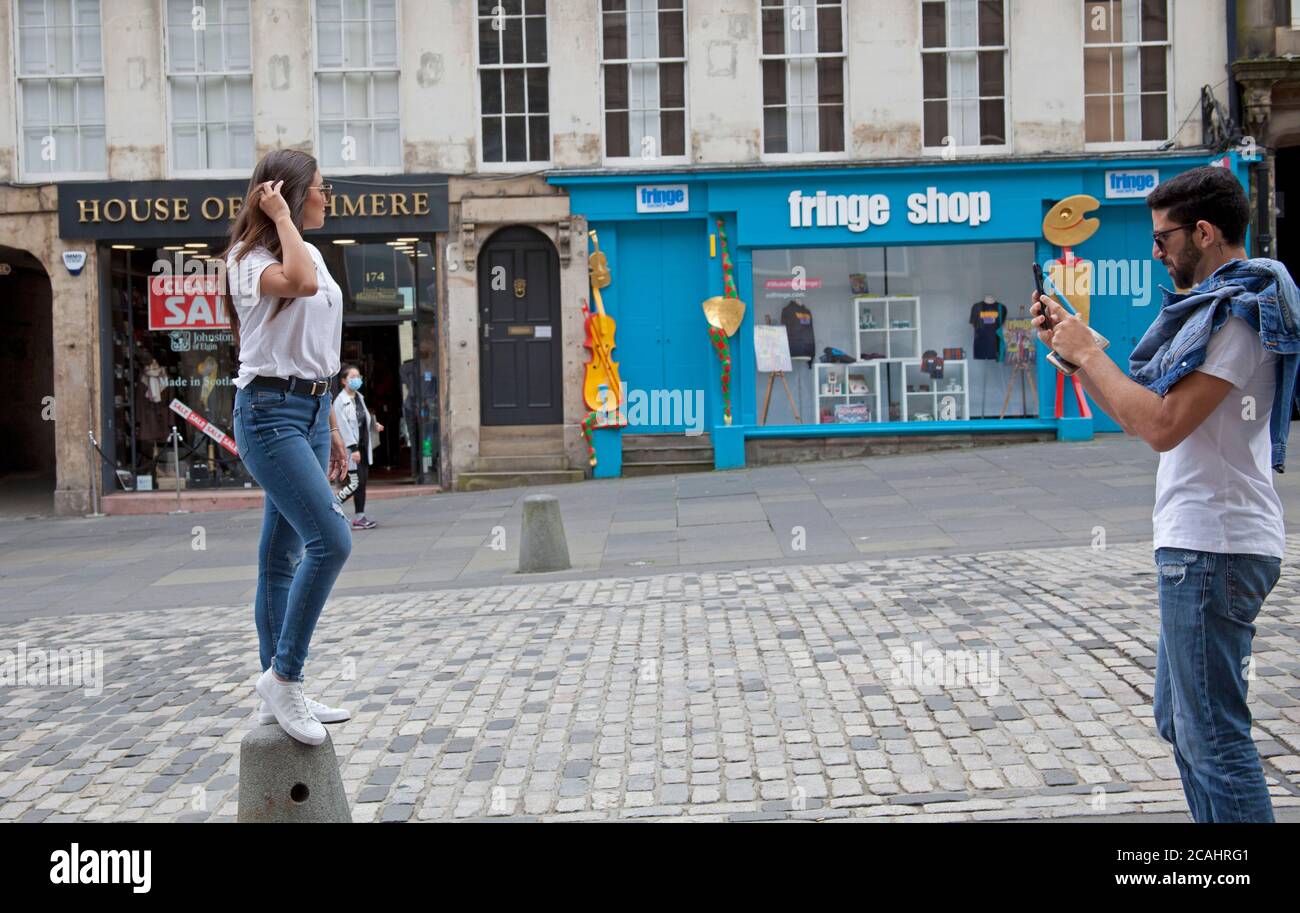 Royal Mile, Edinburgh, Schottland, Großbritannien. August 2020. Bewölkt und schwül 22 Grad. Touristen tröpfeln immer noch in ein einigermaßen ruhiges Stadtzentrum und helfen den Restaurants und Cafés in der schottischen Hauptstadt. Im Bild: Mädchen auf Straßenmöbeln posiert für ein Foto. Stockfoto