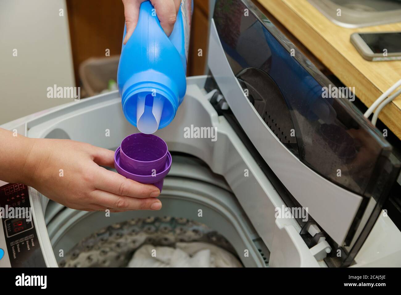 Frau gießt flüssiges Seifenpulver in die Trommel der Waschmaschinenwäsche Stockfoto