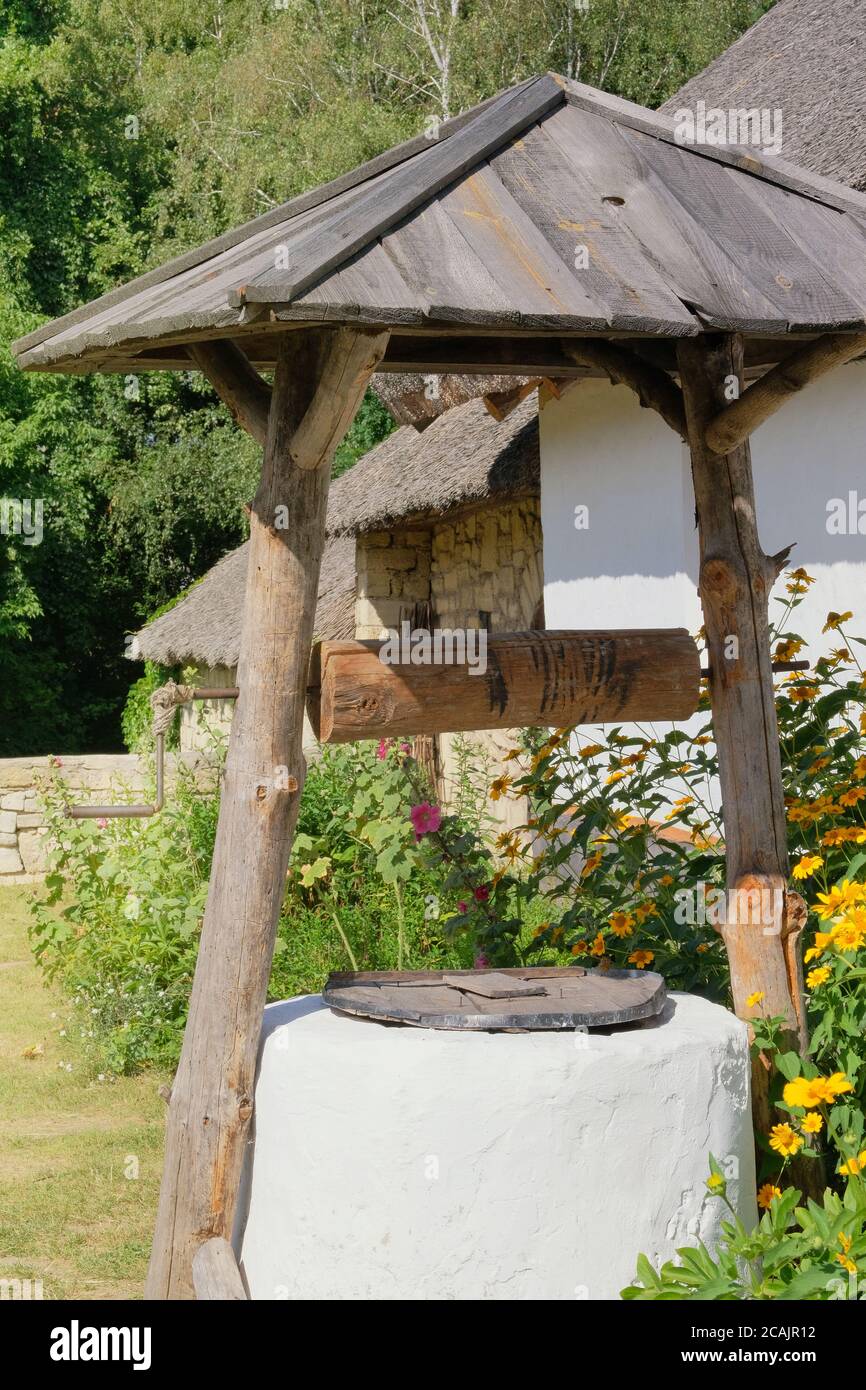 Alter Brunnen in der Nähe einer ländlichen Hütte mit weiß getünchten Wänden. Historisches Dorf in der Ukraine, Erhaltung der Traditionen und Kultur. Stockfoto