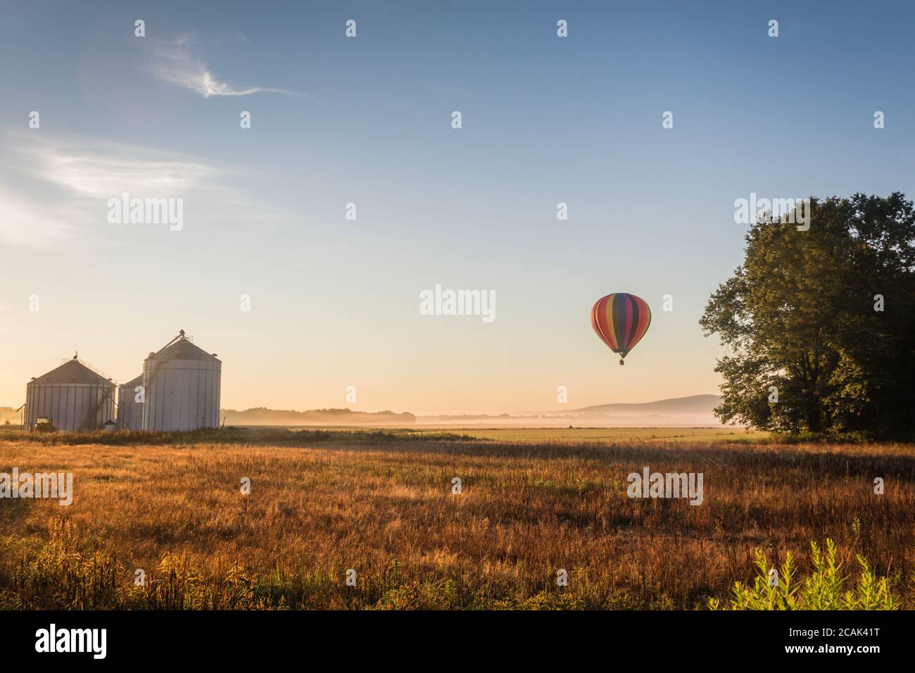 Heißluftballon schwimmt über nebelgefüllten Bauernhof Feld und Sanfte Hügel bei Sonnenaufgang Stockfoto