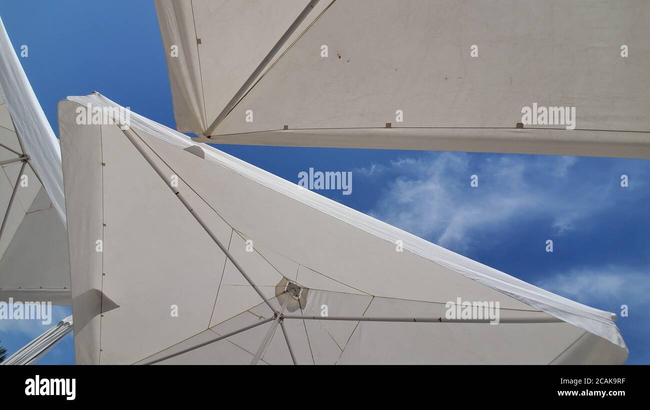 Dreieckige Form Teile von weißen Sonnenschirmen auf hohen blauen Himmel Hintergrund mit hellen weißen Wolken. Aufnahme unter den Sonnenschirmen Stockfoto