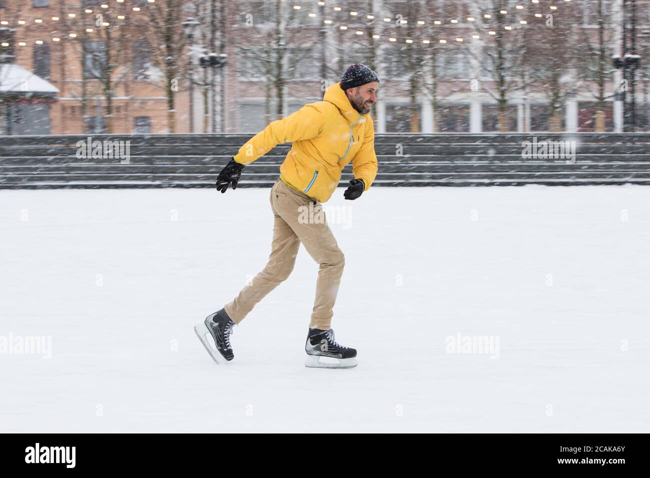 Porträt eines bärtigen Mannes in gelber Jacke, beige Hose, schwarzer Hut  auf Eisbahn, im Winter im Freien, Seitenansicht. Hübscher Mann, der im Mot  schießt Stockfotografie - Alamy