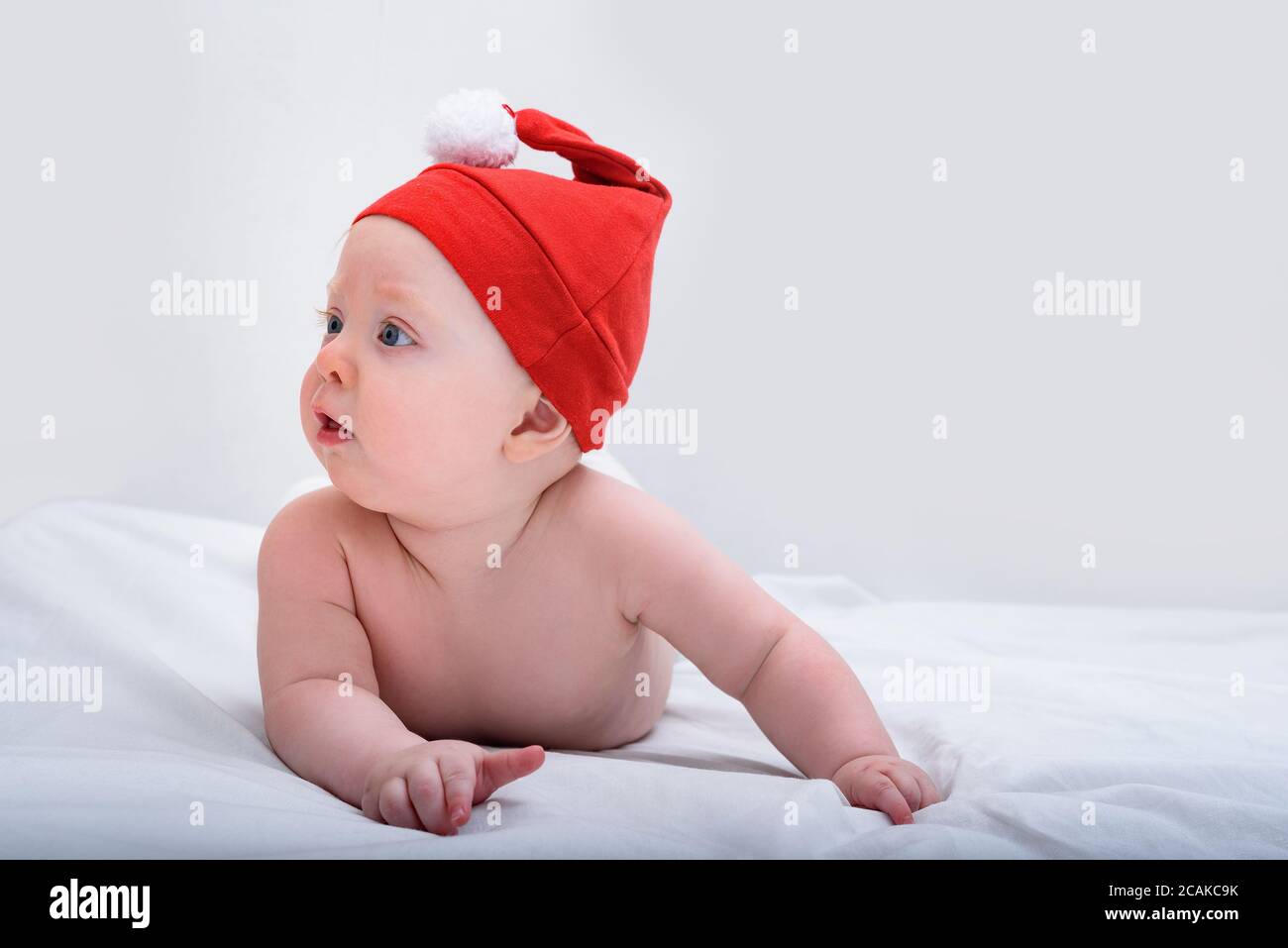 Niedliches kleines Baby im Weihnachtsmütze, das ohne Kleidung auf dem Bauch liegt. Weißer Hintergrund Stockfoto