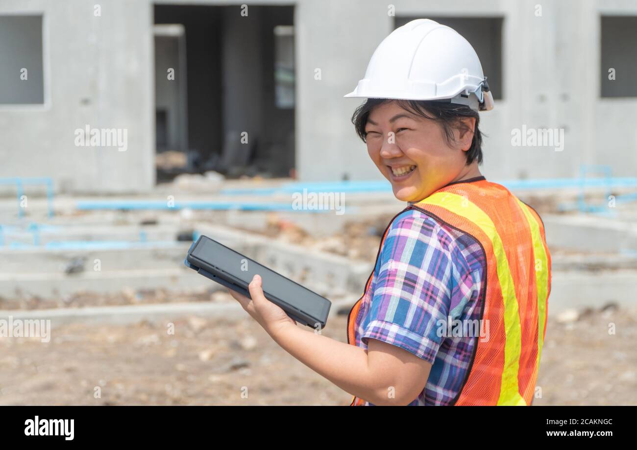 Portrait von asiatische Frau Bauingenieur Arbeiter mit Helm auf dem Kopf mit Tablette beim Stehen auf Baustelle Baustelle auf zurück Stockfoto