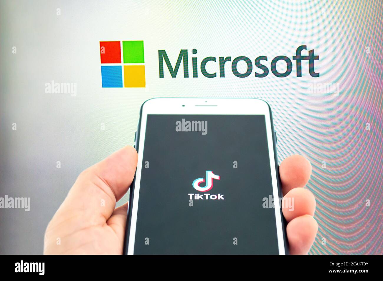 Calgary, Alberta, Kanada. August 2020. Eine Person, die ein iPhone 8 Plus mit dem TikTok-Logo auf einem Monitor mit dem Microsoft-Logo hält. Konzept Microsoft Stockfoto