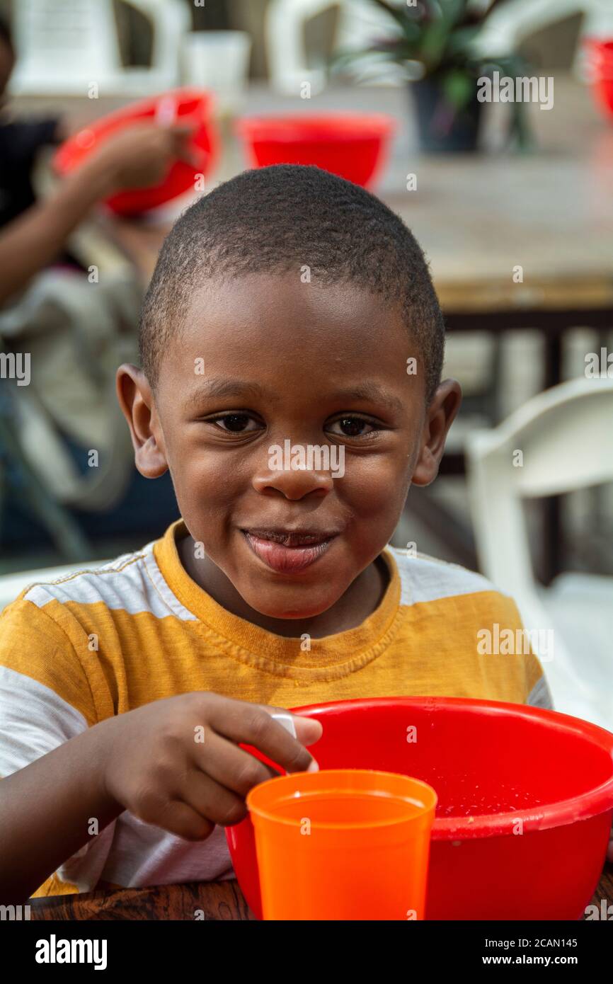 Ein Kind isst seine Suppe auf Basis von Reis, Getreide, Gemüse und manchmal mit Fleisch oder Fisch. Auch ihnen wird ein Glas Milch angeboten. In der Pfarrei Maria Aux Stockfoto