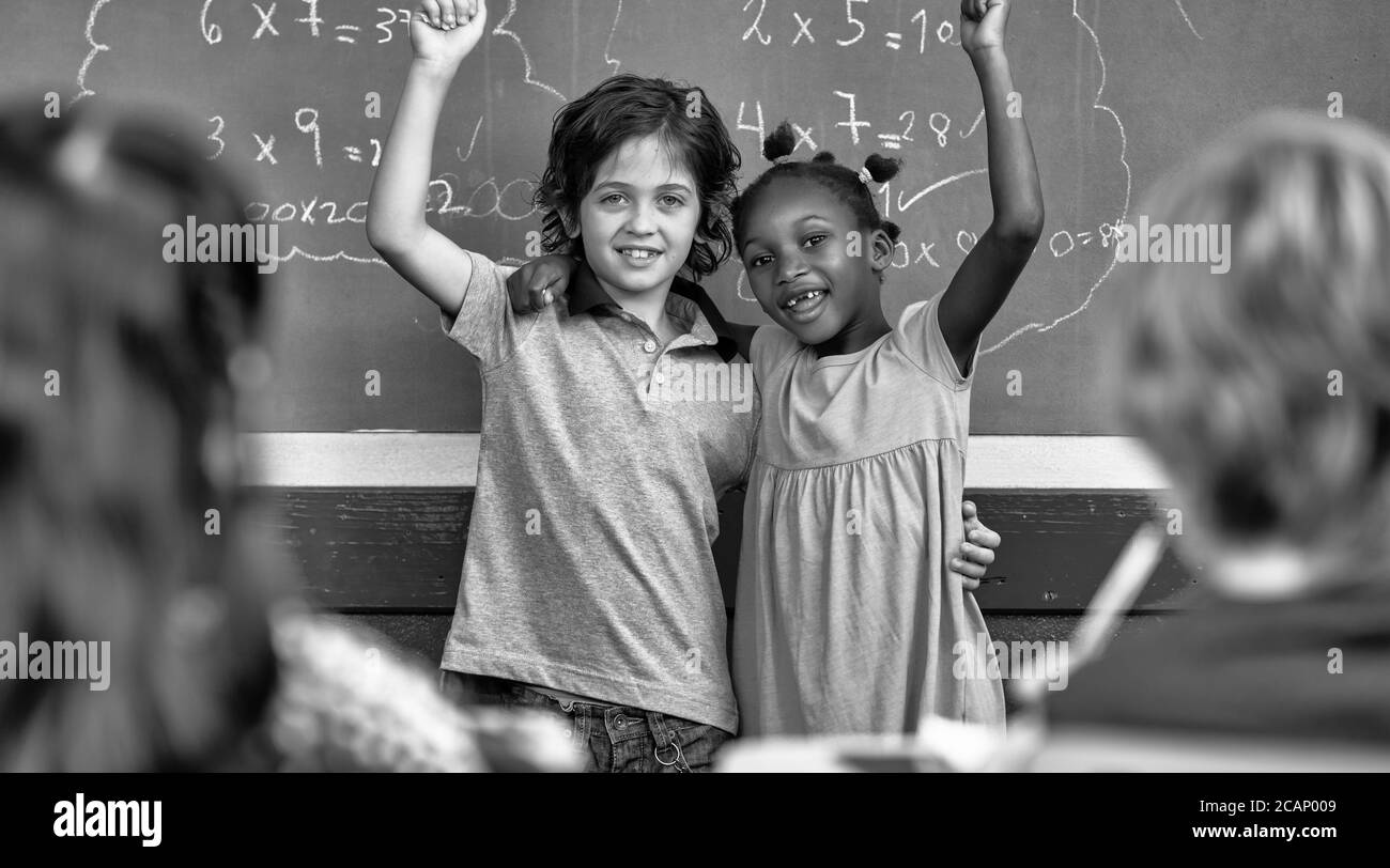 Glückliches afrikanisches Mädchen und kaukasischer Junge umarmen und lächeln an der Tafel des Klassenzimmers. Zurück zur Schule Konzept Stockfoto