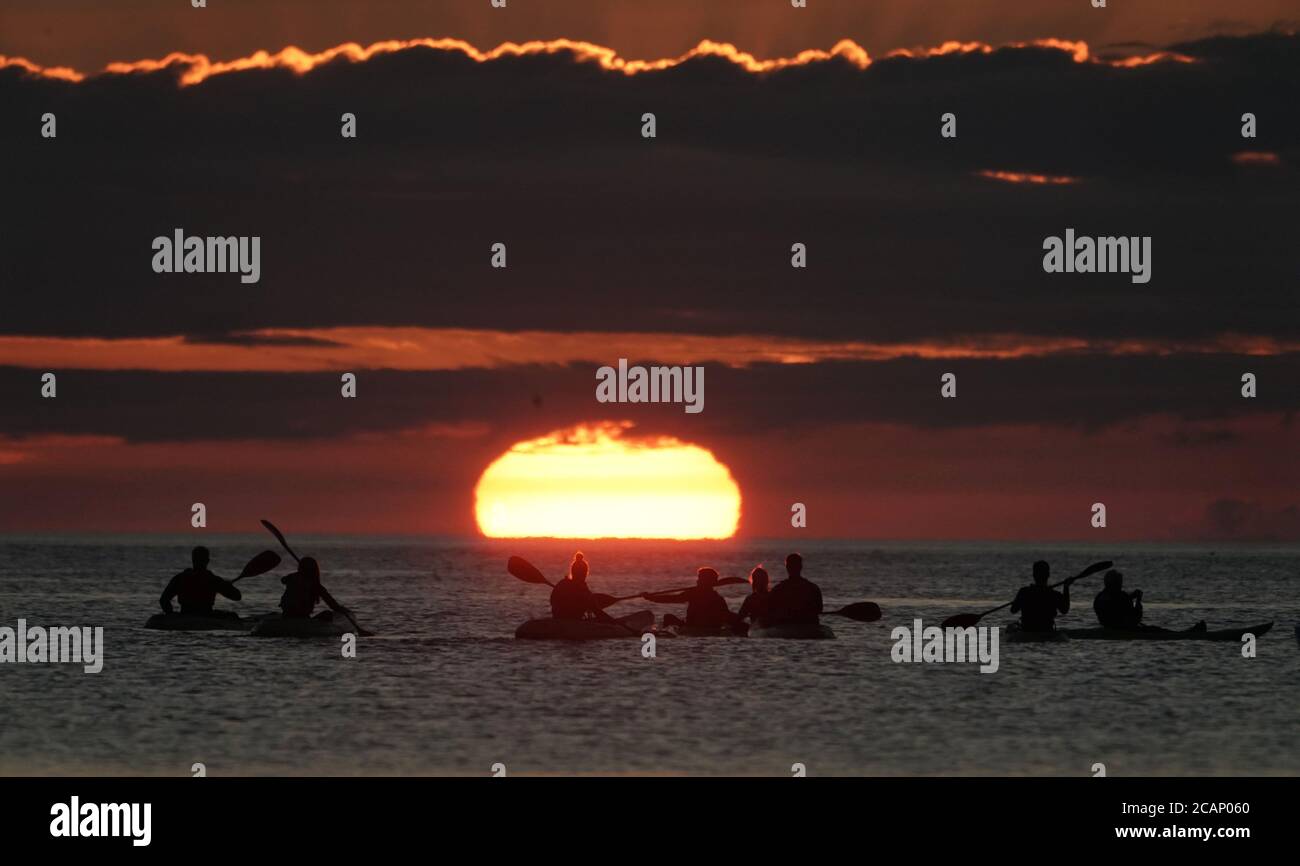 Kajakfahrer beobachten den Sonnenaufgang in der Cullercoats Bay in North Tyneside. Stockfoto