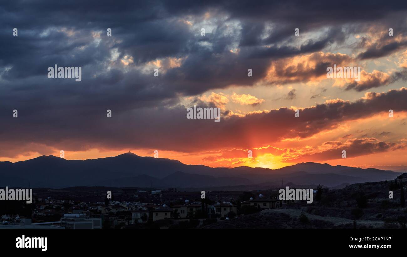 Strahlen von Sonnenlicht kommen durch Sturmwolken in Larnaca, Zypern über einem kleinen Dorf von Bergen umgeben Stockfoto