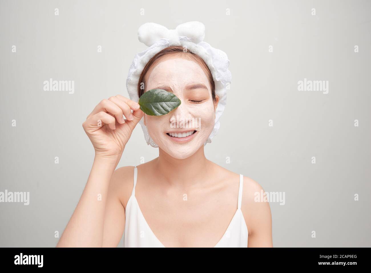Asiatische Frau in Handtuch Anwendung weißen Gesichtsmaske Ton und hält ein Blatt. Stockfoto