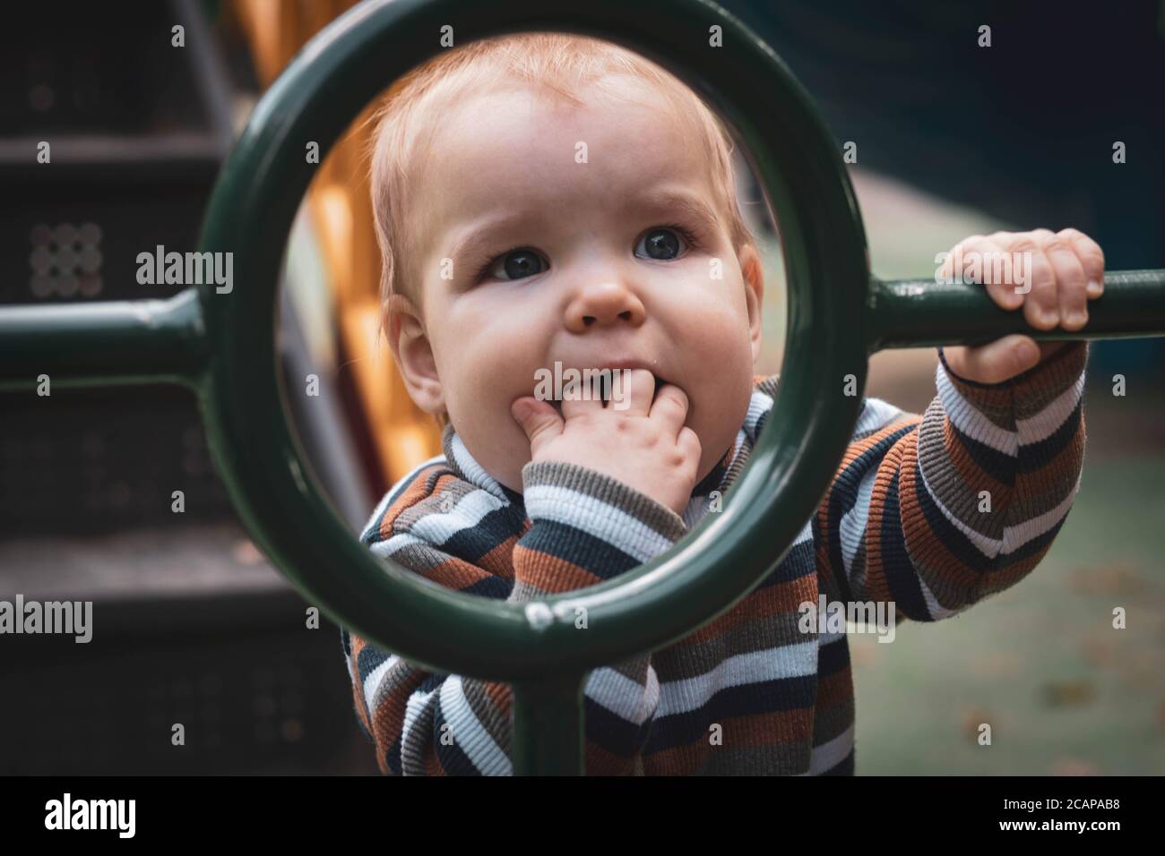 Baby Kind auf dem Spielplatz zieht seine Finger in den Mund. Aufrechterhaltung der Hygiene im Freien. Die schmutzigen Hände des Kindes tragen Bakterien und Viren. Stockfoto