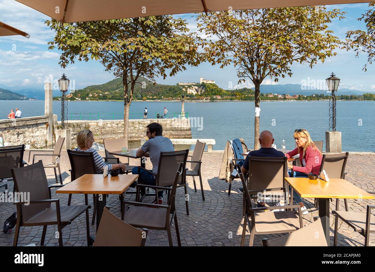 Arona, Piemont, Italien - 25. September 2019: Die Leute sitzen an der Bar und genießen den Blick auf die Rocca Borromea in Angera vom See Stockfoto