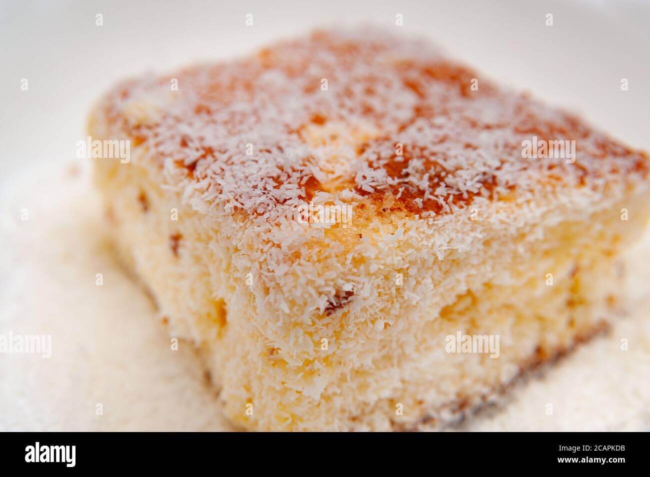 Traditionelles brasilianisches Dessert (bekannt als Bolo Gelado) - Schritt für Schritt: Nahaufnahme des Kuchenstückes mit geriebener Kokosnuss. Selektiver Fokus. Stockfoto