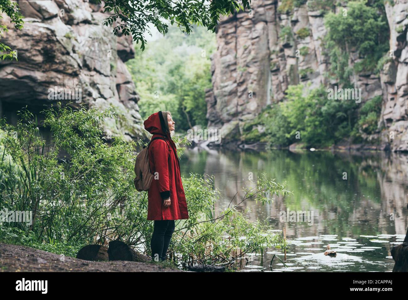 Frau in rotem Mantel neben Steinmauer der Klippe in Buky Canyon, Ukraine Stockfoto