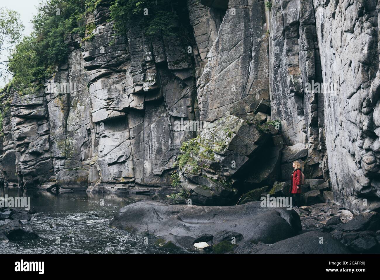 Frau in rotem Mantel neben Steinmauer der Klippe in Buky Canyon, Ukraine Stockfoto