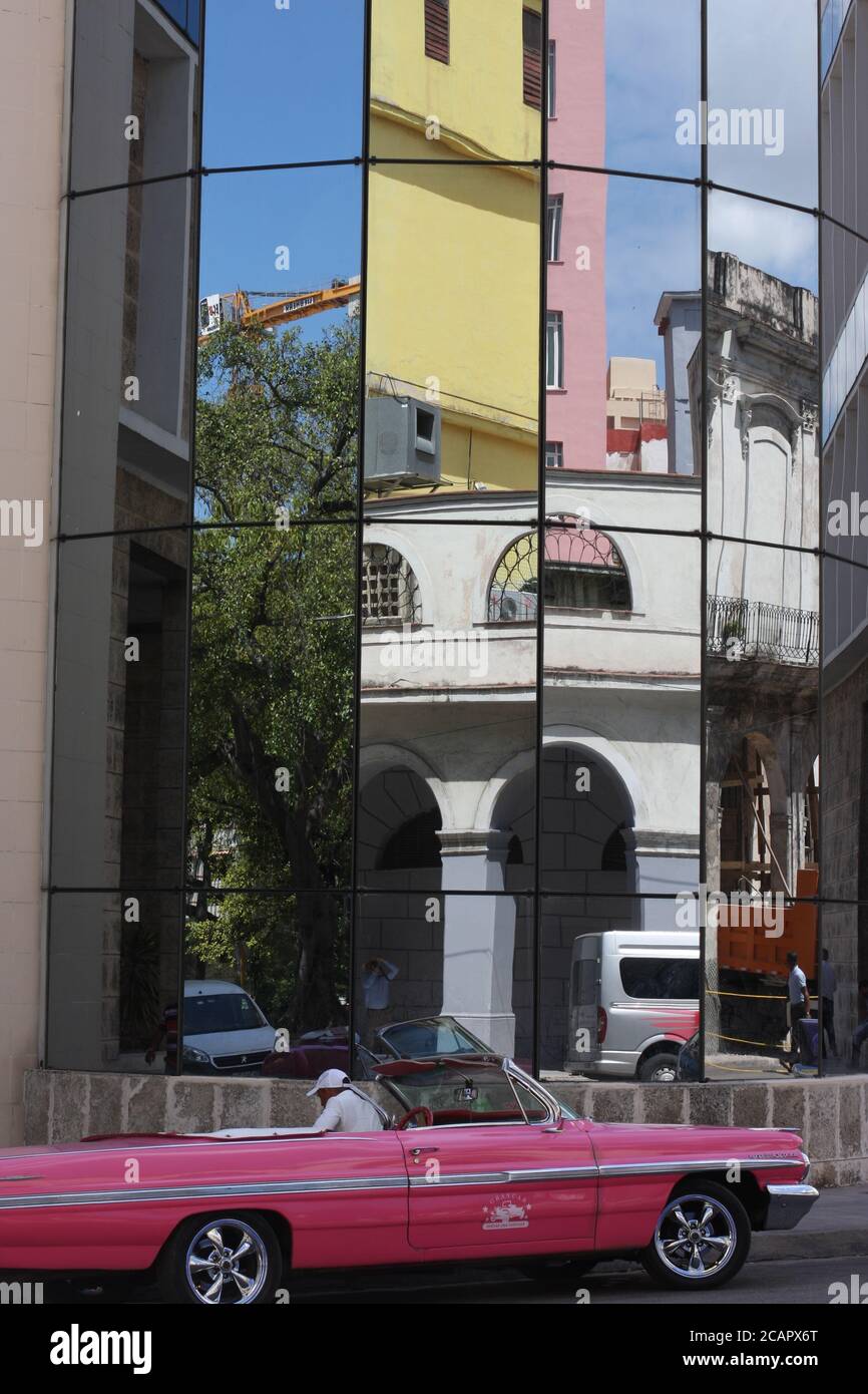 Das rosafarbene Auto der 50er Jahre parkte vor dem modernen Gebäude, das den Rest der Straße, Havanna, Kuba, widerspiegelt Stockfoto