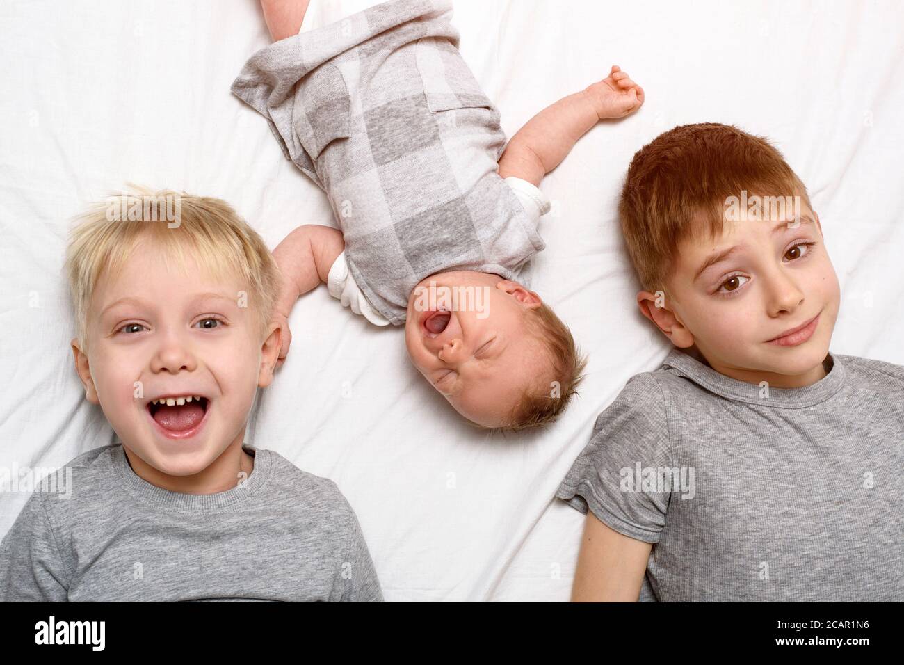 Zwei ältere Brüder und das jüngste Baby in einem weißen Bett. Glückliche Kindheit, große Familie. Draufsicht Stockfoto