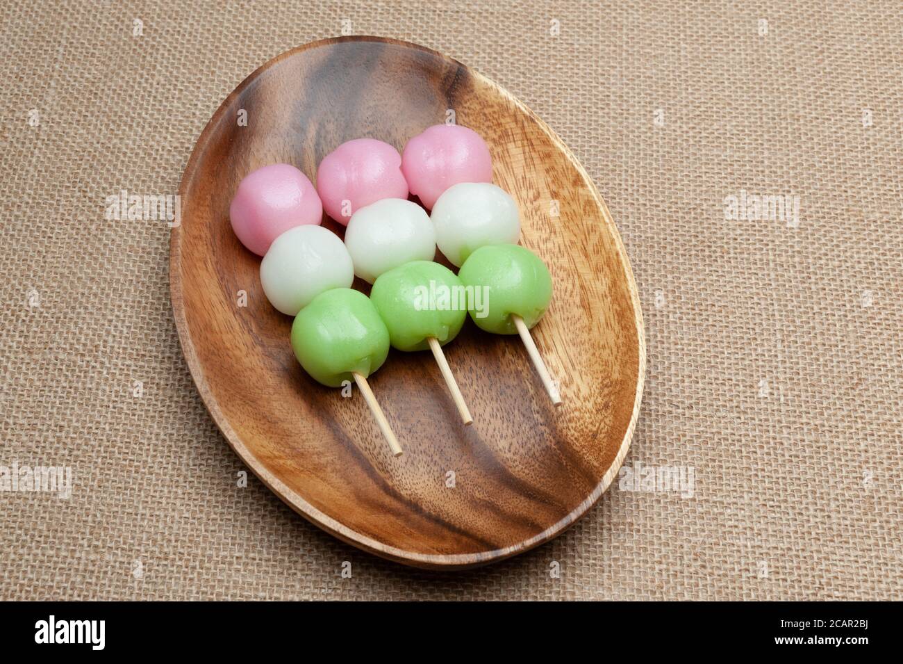 Japanische traditionelle süße Dango Mochi auf Holzplatte genannt. Isoliert auf Jute-Hintergrund. Nahaufnahme. Draufsicht. Speicherplatz kopieren. Stockfoto