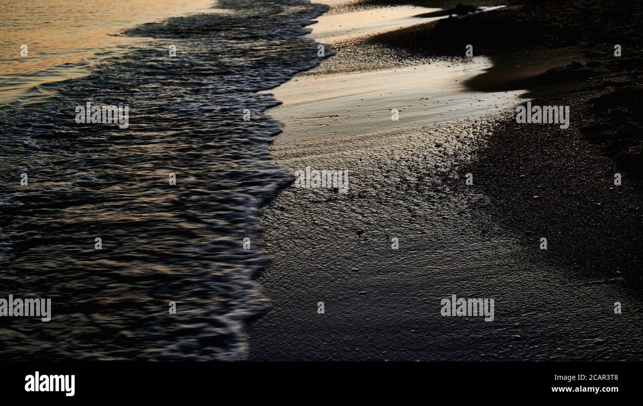 Meeresschaum, Strandlinie bei Sonnenuntergang, nasser Sand, Hintergrund Stockfoto