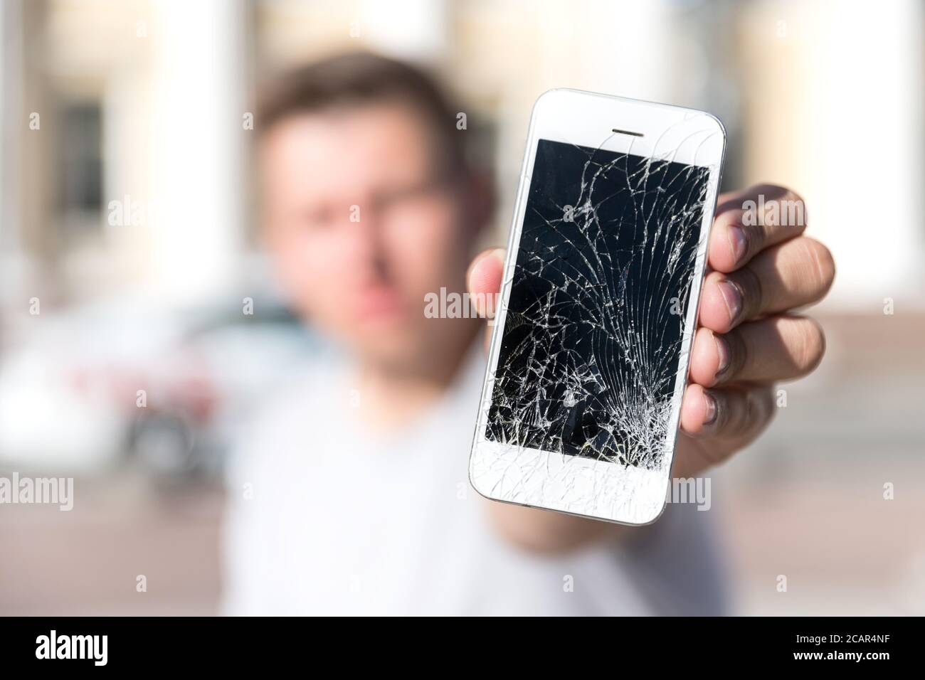 Kaukasischer junger Mann hält und zeigt gebrochenen Smartphone-Bildschirm (Display), selektiver Fokus auf Smartphone, verschwommenes Gesicht, im Freien. Stockfoto Kaukasischer junger Mann hält und zeigt gebrochenen Smartphone-Bildschirm (Display), selektiver Fokus auf Smartphone, verschwommenes Gesicht, im Freien. Stockfoto