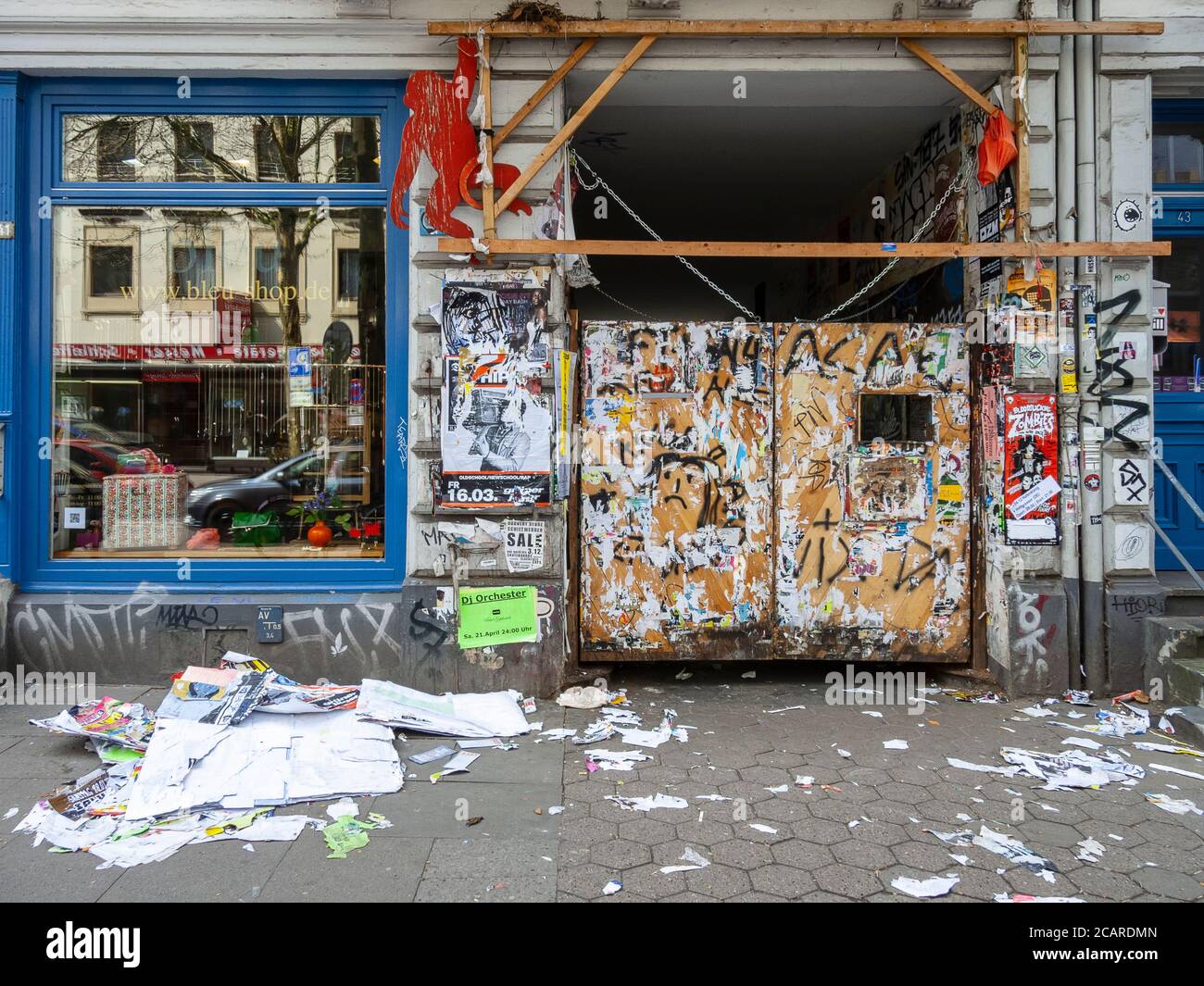Reste von Plakaten und Graffiti an den Türen eines Tores in der Schanzenstraße. Die Plakatreste sind auf dem Bürgersteig, Hamburg, verstreut. Stockfoto