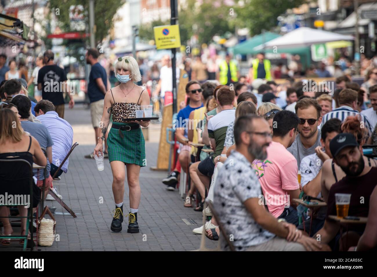 Clapham wartet auf Tische mit einer Gesichtsmask an der Northcote Road und ist nun für Autos gesperrt und öffnet an einem heißen Sommertag die Straße für Restaurants und Bars. Stockfoto