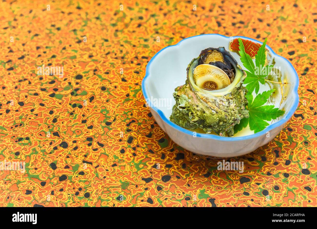 Hochwertige japanische Küche der traditionellen Tsubo-yaki gedämpfte Sazae gehörnte Turban Meeresschnecke in einem Teller mit Ahorn Momiji Blätter dekoriert. Stockfoto