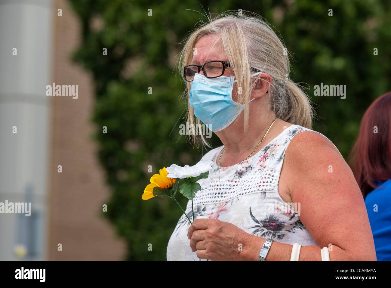 Weiße kaukasische weibliche Falten Blumen platziert werden, um das Gesundheitspersonal getötet durch COVID-19 in Basildon, Essex, Großbritannien zu ehren. Emotionaler Service Stockfoto
