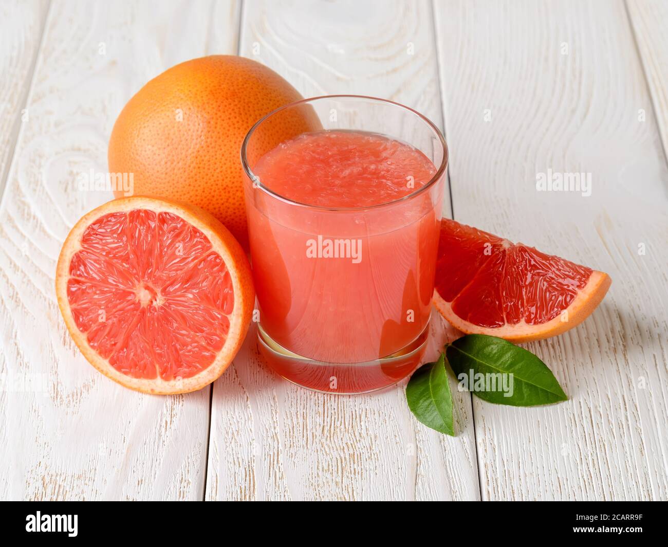 Glas frisch gepresster Grapefruitsaft mit Fruchtfleisch und ganzen, halb und Viertel Grapefruits auf einem weißen Holztisch. Vegetarische, Rohkost Ernährung. Stockfoto