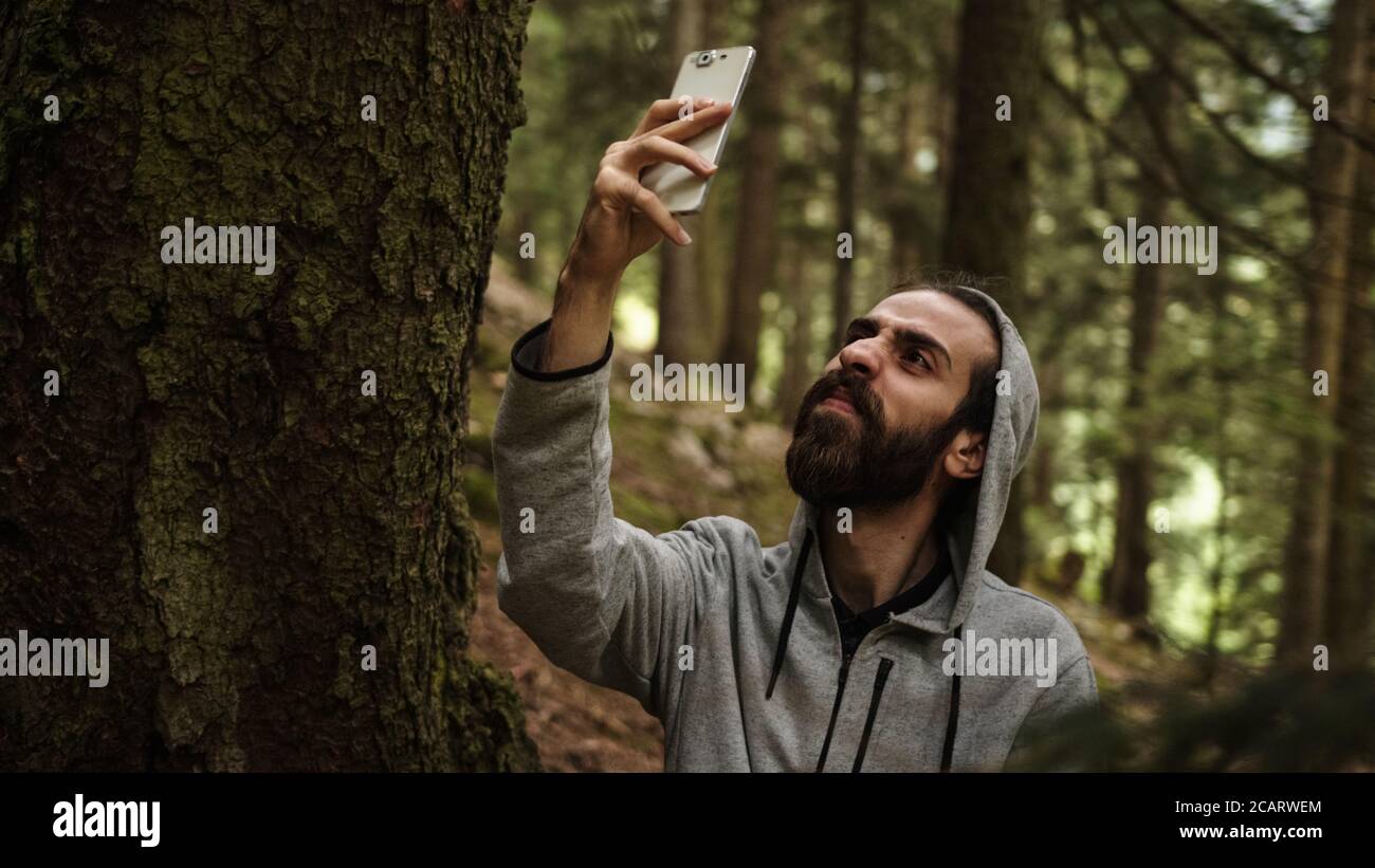 Hipster Teenager SMS im Wald mit einem Telefon in der Hand bricht das Signal, betonte jungen Mann mit Signalproblemen Stockfoto