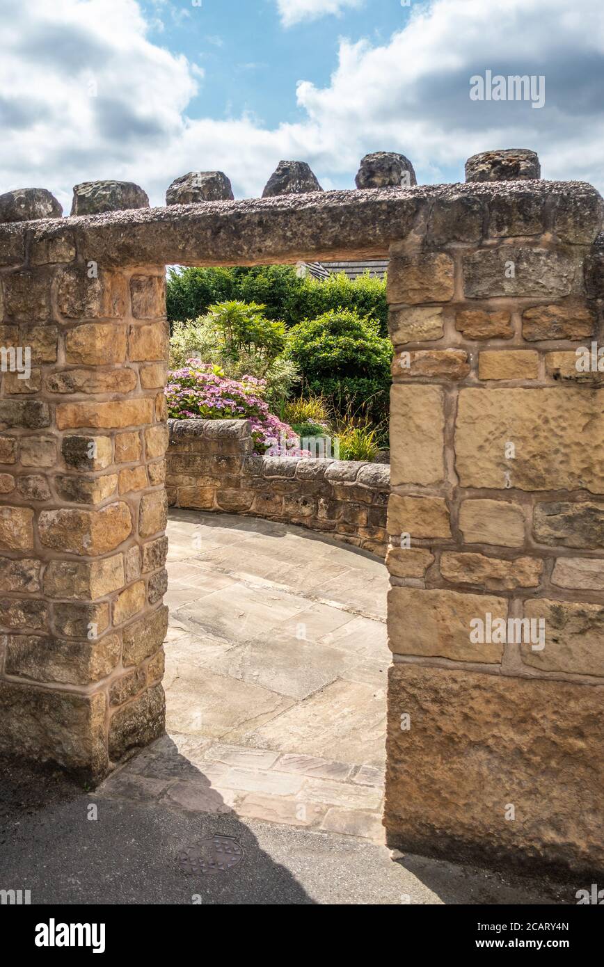 Steinmauer mit Torbogen in Stein, der zu einem Garten führt Stockfoto